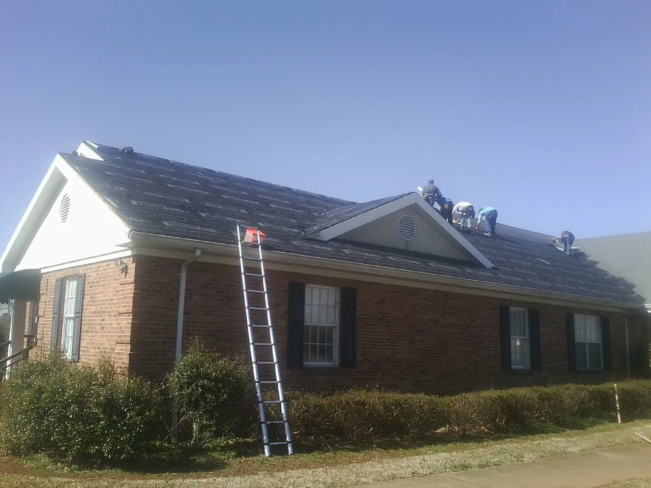 Crew tearing shingles off a brick ranch roof with a ladder set — Metal Roof Repair work by our crew in Circle Pines