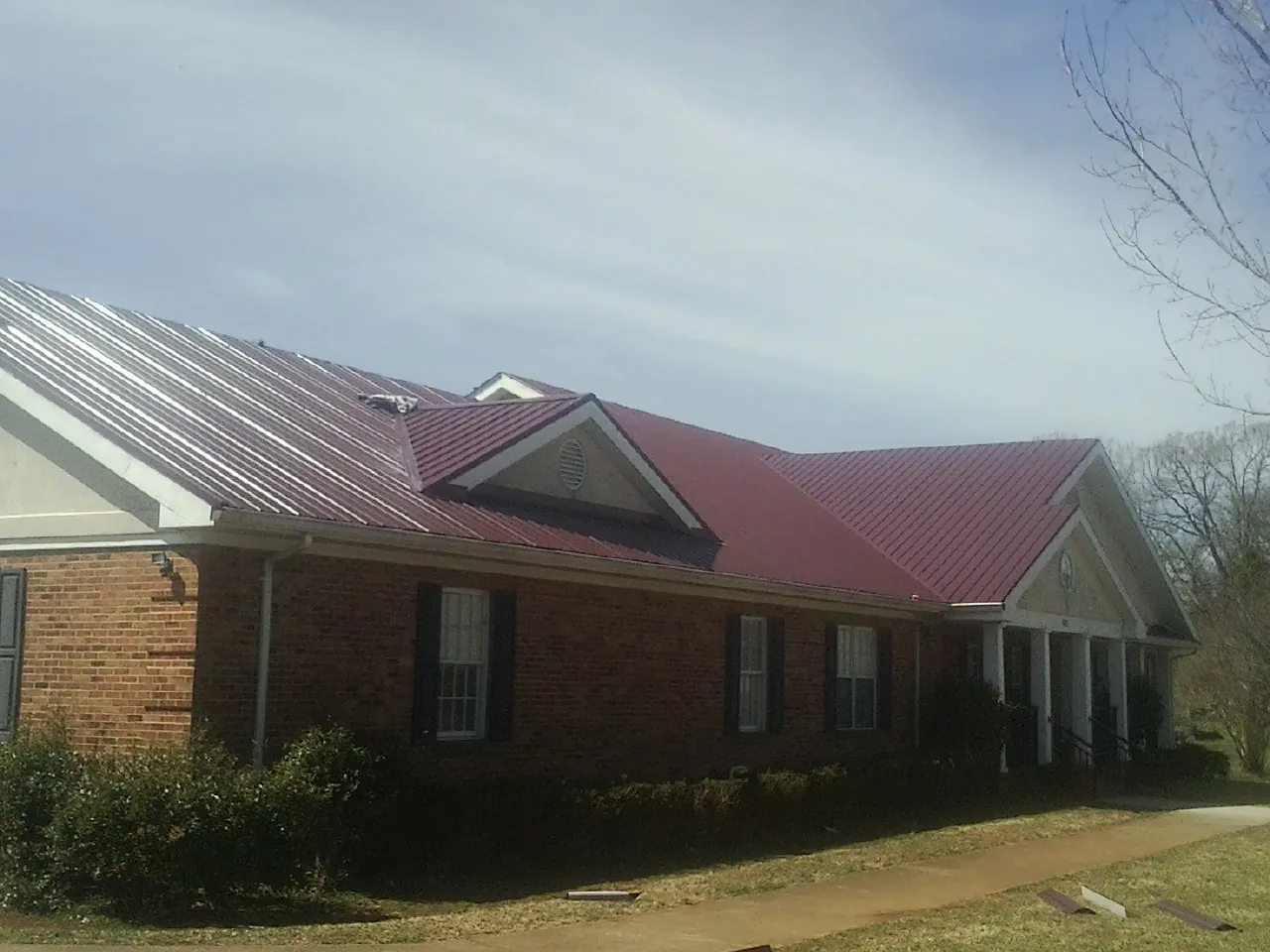 Red metal roof with gabled entries on a long brick building, from a Hail Damage Roof Repair job in Circle Pines