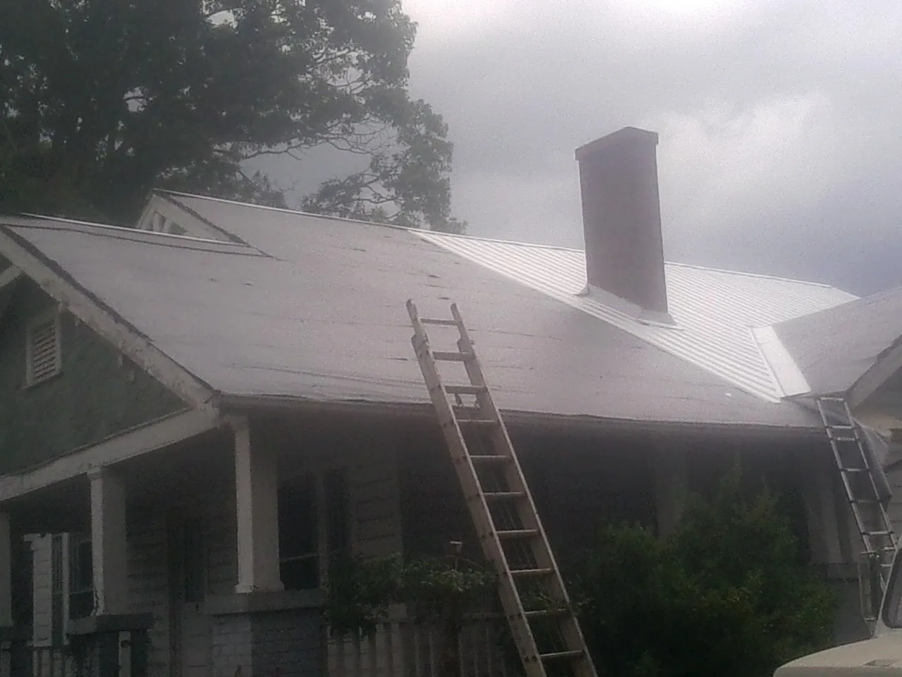 Ladders against a metal roof on an older home with a brick chimney in Circle Pines