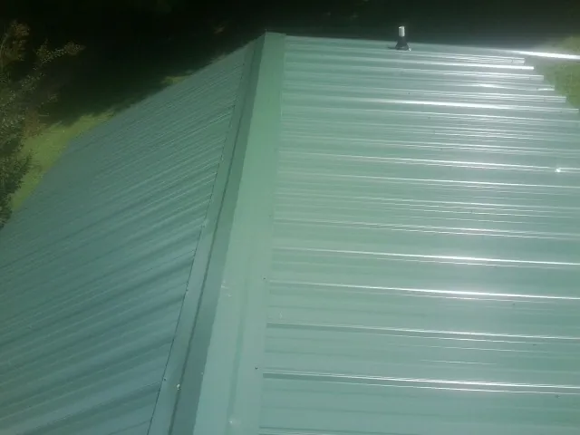 New green metal panels meeting at the ridge of a roof — Flat Roof Repair work by our crew in Circle Pines