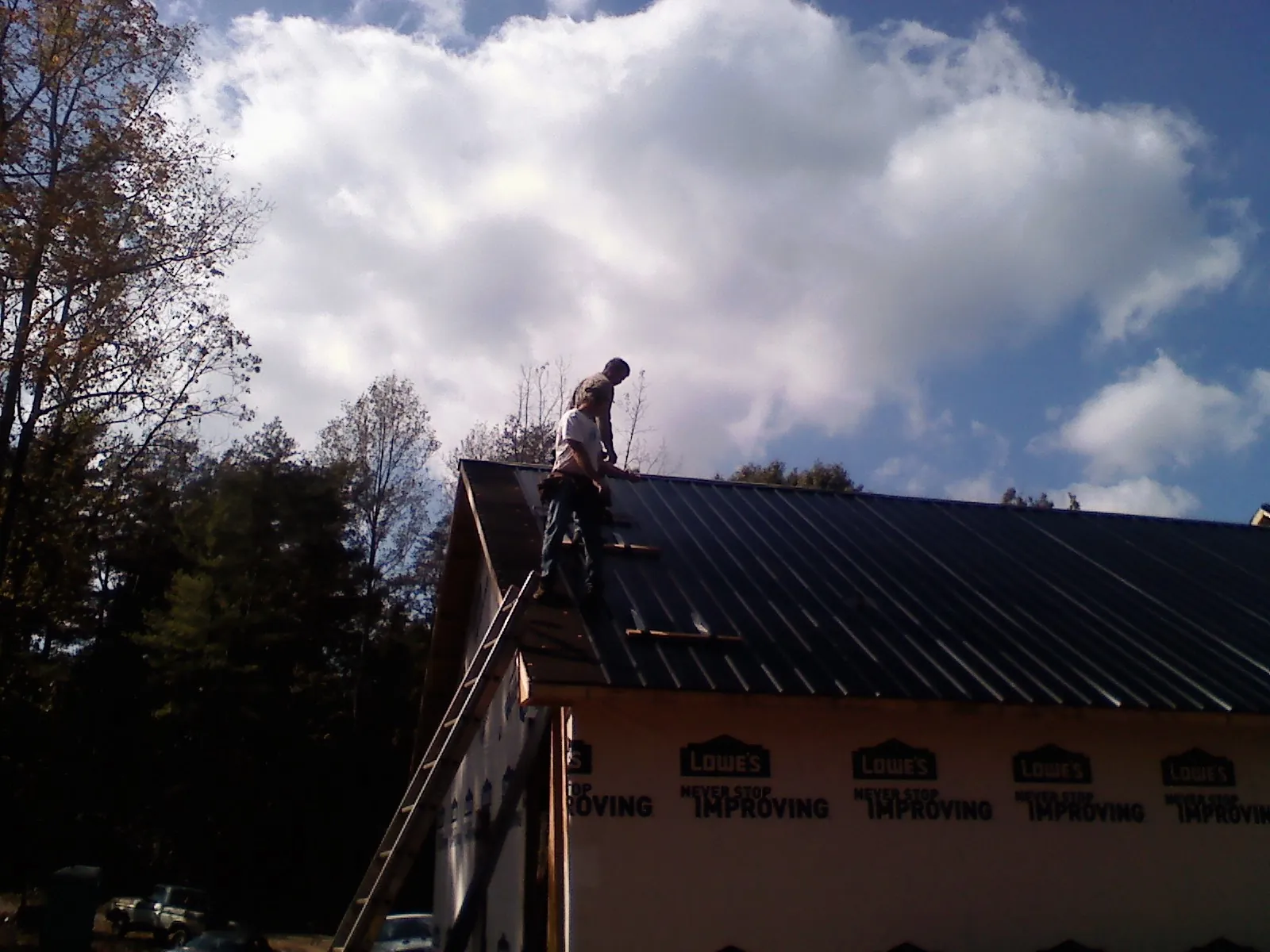 Roofer fastening dark metal panels high against a cloudy sky, from a Roof Inspection job in Circle Pines