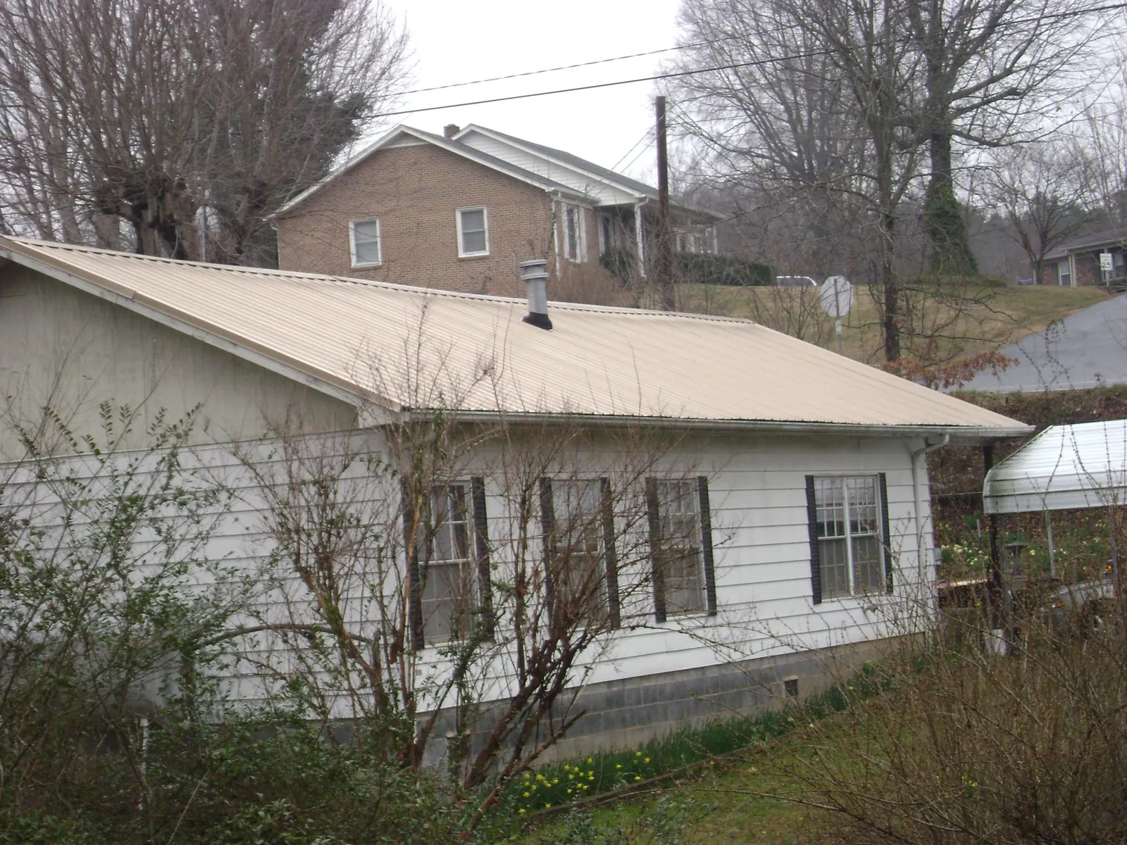 Tan metal roof on a white sided house set into a hillside — Commercial Roofing by Roofing Brothers in Circle Pines